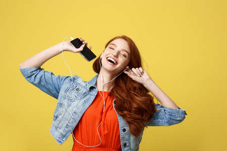 Lifestyle and Music Concept: Beautiful young curly red hair woman in headphones listening to music and dancing on vivid yellow backgroundの写真素材