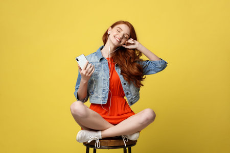 Lifestyle, Music, Technology concept: Young beautiful caucasian woman listening music with headphones and smart phone hand hold, dancing, eyes closed smiling, Isolated on yellow vivid background.の写真素材