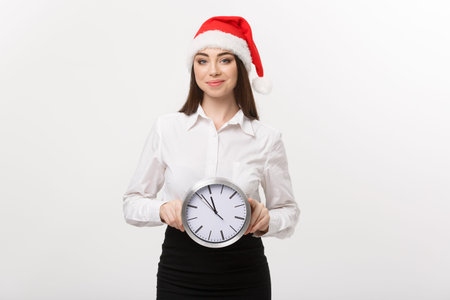 Time management concept - Young happy business woman with santa hat holdinga clock isolated over...