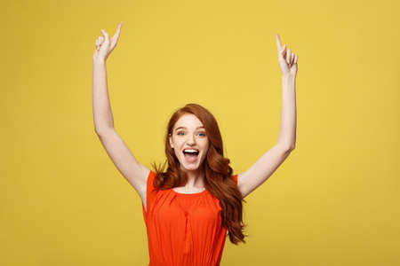 Portrait of redhead young attractive woman pointing to interesting space. Isolated over bright yellow.の写真素材