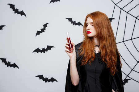 Halloween witch concept - Happy Halloween Witch drinking blood over dark grey studio background with bat and spider web.の写真素材