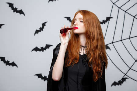 Halloween witch concept - Happy Halloween Witch drinking blood over dark grey studio background with bat and spider web.の写真素材
