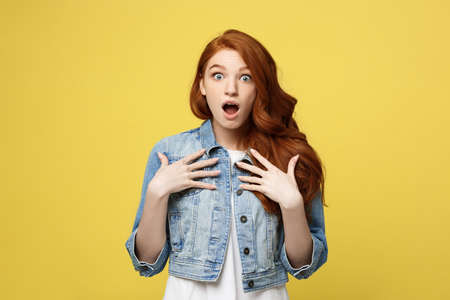 Close up Portrait young beautiful attractive redhair girl shocking with something. Golden yellow Background. Copy space.の写真素材