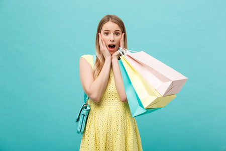 Lifestyle Concept: Portrait shocked young brunette woman in yellow summer dress posing with shopping...