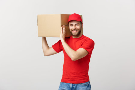 Deliver Concept: Young caucasian handsome delivery man holding a box on shoulder. Isolated over grey...