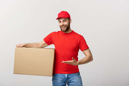Delivery Concept - Portrait of Happy Caucasian delivery man pointing hand to present a box package. Isolated on Grey studio Background. Copy Space.の写真素材
