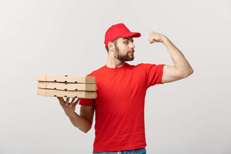 Delivery Concept - Portrait of Strong handsome delivery man flexing his muscle and holding pizza box packages. Isolated on Grey studio Background. Copy Space.の写真素材
