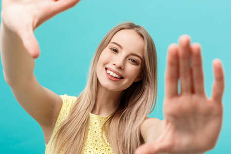 Close-up Young Caucasian woman face and eye care and she making frame with hands isolated over pastel blue background.の写真素材
