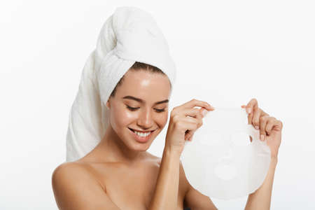 Beauty Skin Care Concept - Beautiful Caucasian Woman applying paper sheet mask on her face white background.の写真素材