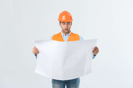 Shocked builder construction worker is holding in hand a plan draft document isolated on gray background.の写真素材