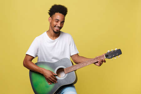 Happy african american musician man posing with a guitar, over golden yellow background.の写真素材