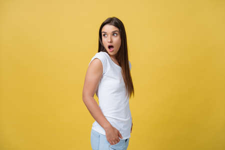 Beautiful female half-length portrait isolated on yellow studio backgroud. The young emotional smiling and surprised woman standing and looking at camera.The human emotions, facial expression conceptの写真素材