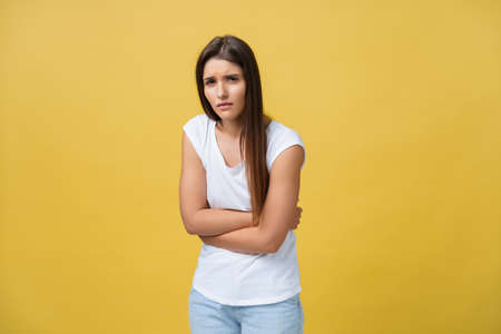 Indoor portrait of cute girl standing with crossed hands on belly, feeling awkward or suffering from pain while looking aside, standing against yellow background. Woman has stomachacheの写真素材