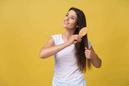 Portrait of beautiful young woman combing her hair, looking at camera and smiling.の写真素材