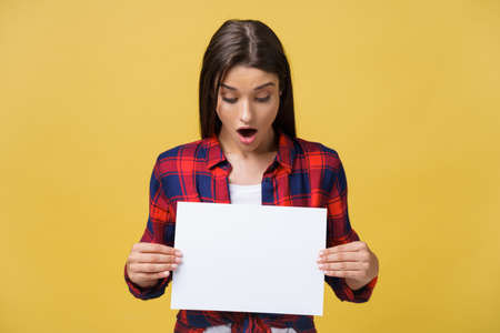 surprised young girl in red shirt with white placard paper in hands isolated on yellow background.の写真素材
