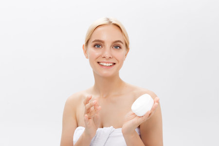 Close up beauty portrait of a laughing beautiful half naked woman applying face cream isolated over...