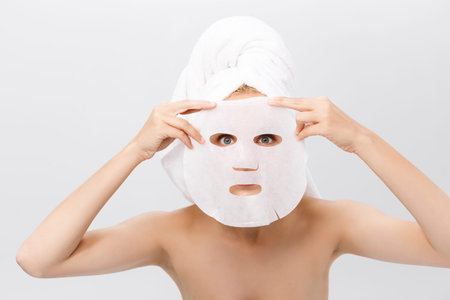 Beauty Skin Care Concept - Beautiful Caucasian Woman applying paper sheet mask on her face white...