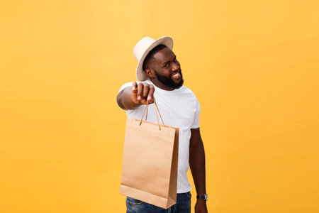 Happy african american man holding shopping bags on yellow background. Holidays concept