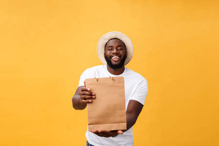 Happy african american man holding shopping bags on yellow background. Holidays conceptの写真素材