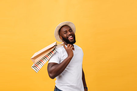 Happy african american man holding shopping bags on yellow background. Holidays concept