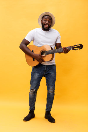 Full-length photo of excited artistic man playing his guitar in casual suite. Isolated on yellow...