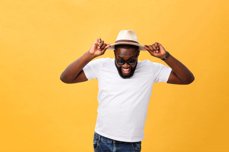 Close up portrait of a young man laughing with hands holding hat isolate over yellow background