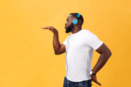 Young African American man wearing headphone and enjoy music dancing over yellow gold Background