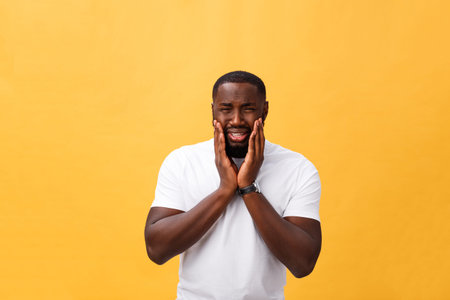 Young Stressed man with hand on his face showing sadness and despair. Isolated over yellow...