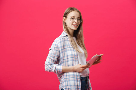 Portrait of a laughing woman using tablet computer isolated on a pink background and looking at...