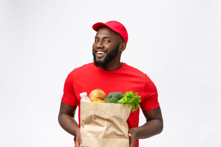 Delivery Concept - Handsome African American delivery man carrying package grocery food and drink from store. Isolated on Grey studio Background. Copy Space.の写真素材