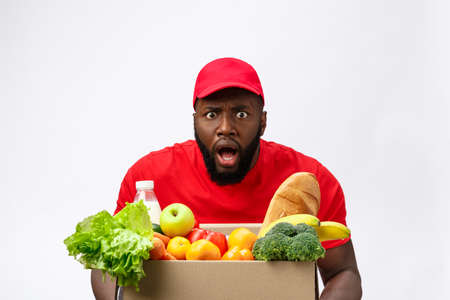 Young african american man holding grocery box in hands with shocking face. Isolated over Grey background.の写真素材
