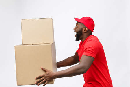 Portrait of delivery african american man in red shirt. he lifting heavy weight boxes against having a isolated on the white background.の写真素材