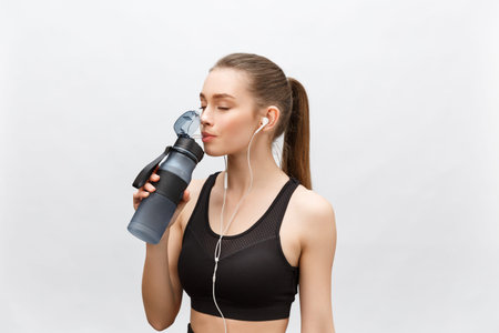 Attractive relaxed young woman with drinking water and listening to music over white background.