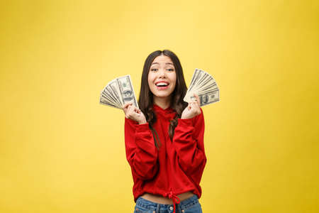 Closeup of young beautiful woman with us dollar money in hand over yellow background, with copy spaceの写真素材