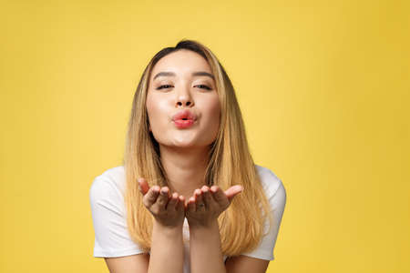 Beautiful young Asian woman blow a kiss isolated on yellow backgroundの写真素材