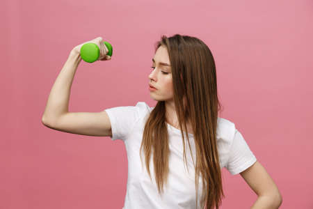 Fitness, young woman with dumbbells at studio background. Pretty girl isolate over pinkの写真素材