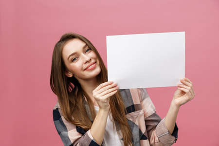 Close up portrait of positive laughing woman smiling and holding white big mockup poster isolated on pink backgroundの写真素材