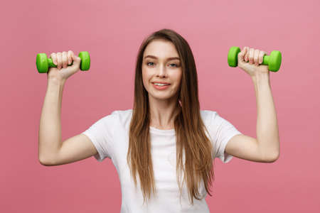 Fitness, young woman with dumbbells at studio background. Pretty girl isolate over pinkの写真素材