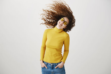 Young girl standing isolated on grey wall playing around looking camera smiling happy close-up