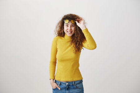 Young girl standing isolated on grey wall playing around looking camera smiling happy close-up