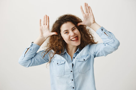Young girl standing isolated on grey wall playing around looking camera smiling happy close-up