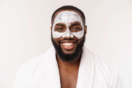 Young african-american guy applying face cream on white background. Portrait of a young happy smiling african man at studio. High fashion male model.の写真素材