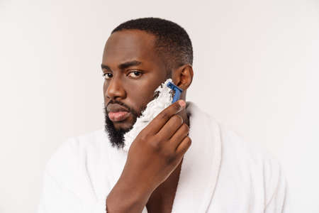 African American man smears shaving cream on face by shaving brush. Male hygiene. Isolated on white background. Studio portraitの写真素材