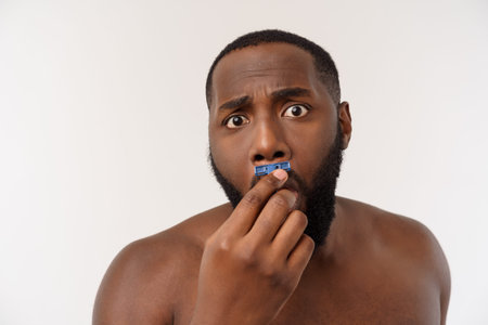 Close up of a happy naked african man shaving with razor isolated over gray background