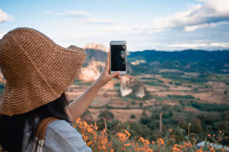 The girl take photo with smart phone on balcony bar at Phu Lang Ka mountain landmark in Phayao province Thailand.の写真素材