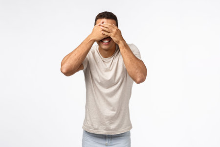 Handsome masculine young man playing hide-n-seek or peekaboo, cover eyes, standing blindfolded and...