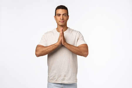 Peaceful good-looking strong, athletic young man in casual t-shirt, press hands together over chest in namaste, nirvana pose, look patient and calm, release stress in meditation, practice yogaの写真素材