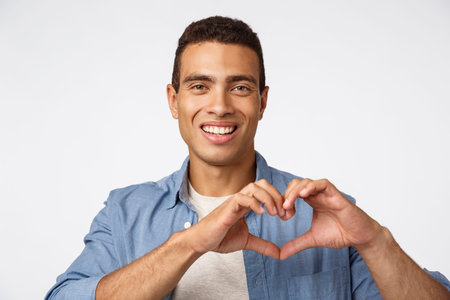 Love, cherity and affection concept. Charming young brazilian masculine man showing heart sign and smiling happy, make surprise dinner for valentines day, arrange christmas romantic nightの写真素材