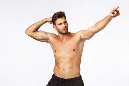 Sexy masculine man with six packs, standing bodybuilder pose naked torso white background, raising hand and pointing right, bragging how got fit in gym, got strong and handsome with exercisesの写真素材