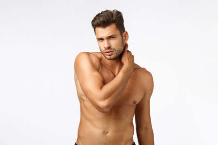 Sport, gym and abs concept. Handsome young gay man taking care body, workout, sportsman standing naked torso, touching neck and looking camera seducative and sexy, white backgroundの写真素材